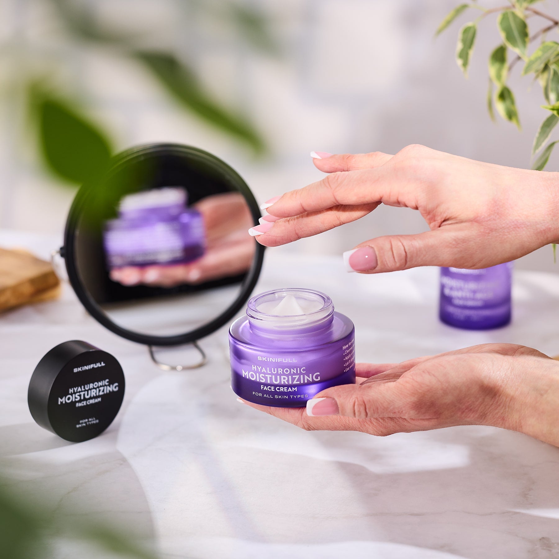 Rankos atidaro Skinifull Hyaluronic Moisturizing Face Cream ir paima priemonę, šalia veidrodėlis