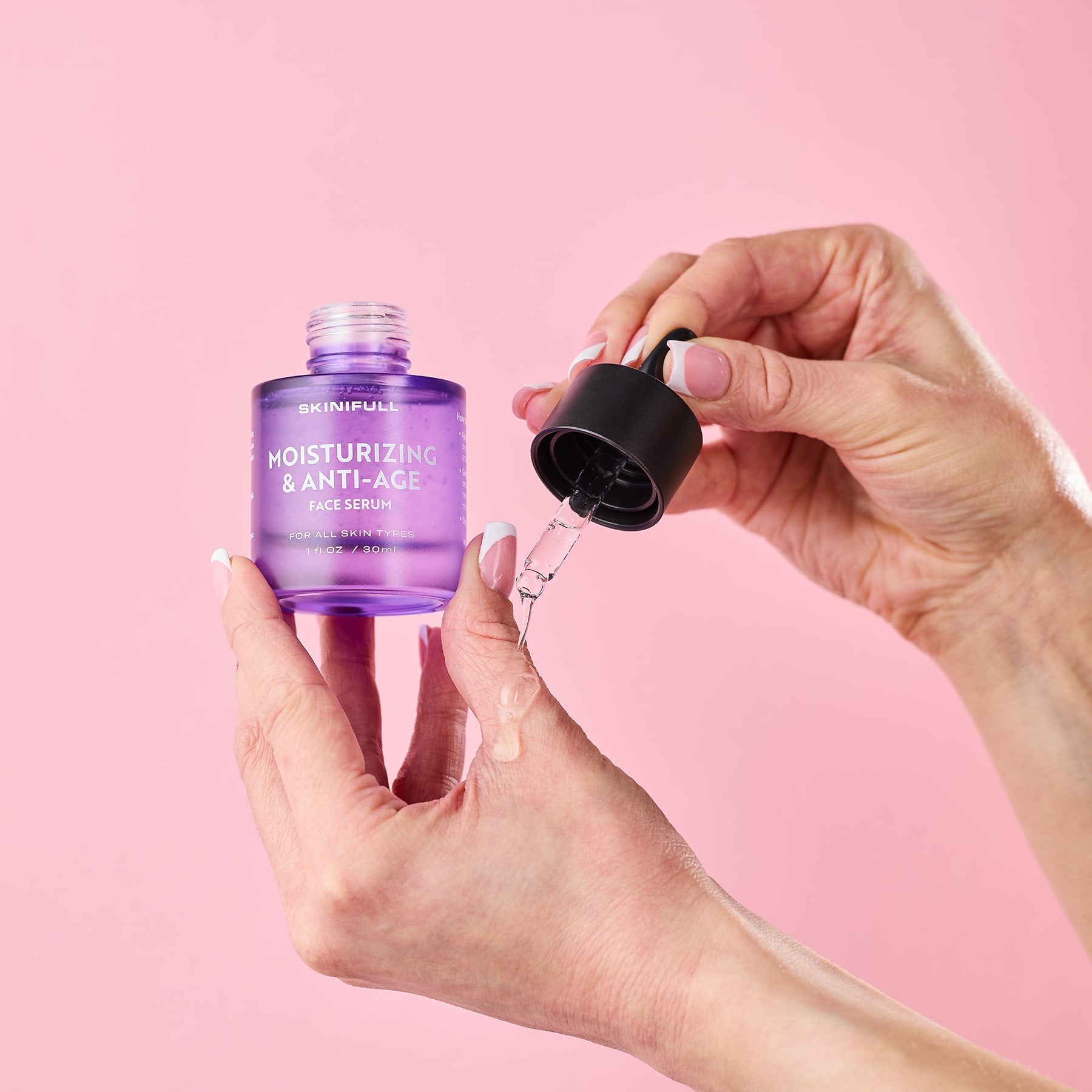 Skinifull Moisturizing & Anti-Age Face Serum – pipete lašinamas serumas ant rankos odos, rožiniame fone